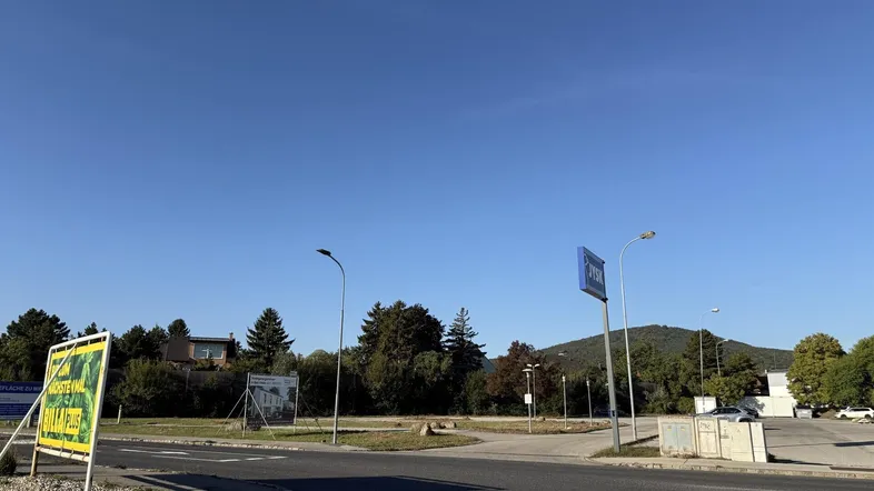 Eine weite Außenansicht mit einer Straße, einem Parkplatz und grünen Bäumen unter klarem blauem Himmel.