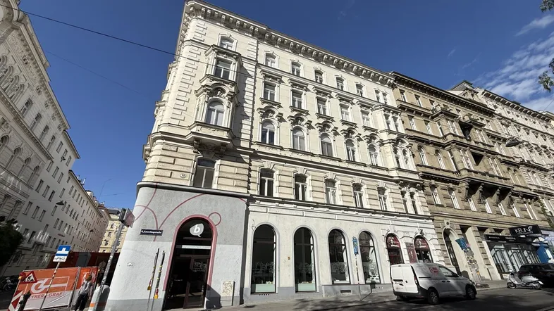 Historisches Eckgebäude mit klassischer Architektur und Geschäften im Erdgeschoss an einer belebten Straße.