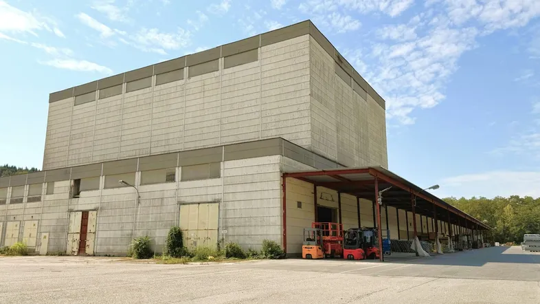 Großes Industriegebäude mit Laderampen und weitläufigem Vorplatz unter blauem Himmel.