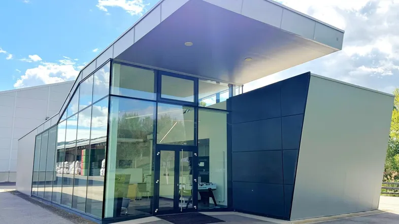 Moderne Architektur mit großer Glasfassade und markantem Vordach unter blauem Himmel.