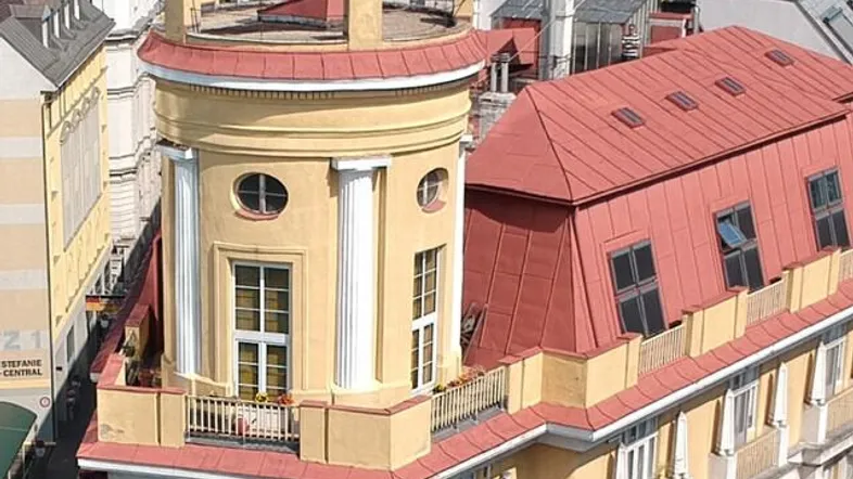 Luftaufnahme eines historischen Gebäudes mit gelber Fassade, rotem Dach und markantem Rundturm in der Stadt.