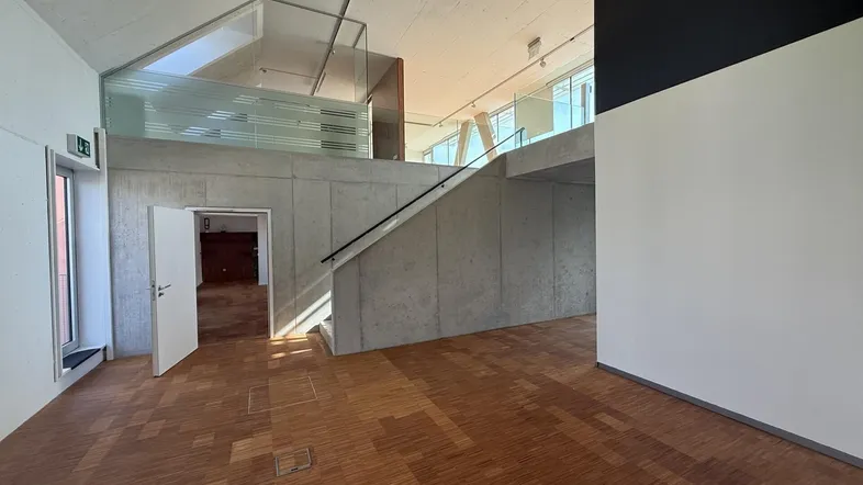 Geräumiger, offener Innenbereich mit hohen Decken, Holzparkettboden und einer modernen Treppe mit Glasgeländer.