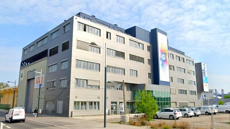 Modernes Bürogebäude mit mehreren Etagen und großen Fenstern an einer Straße, das eine zeitgemäße Architektur aufweist.