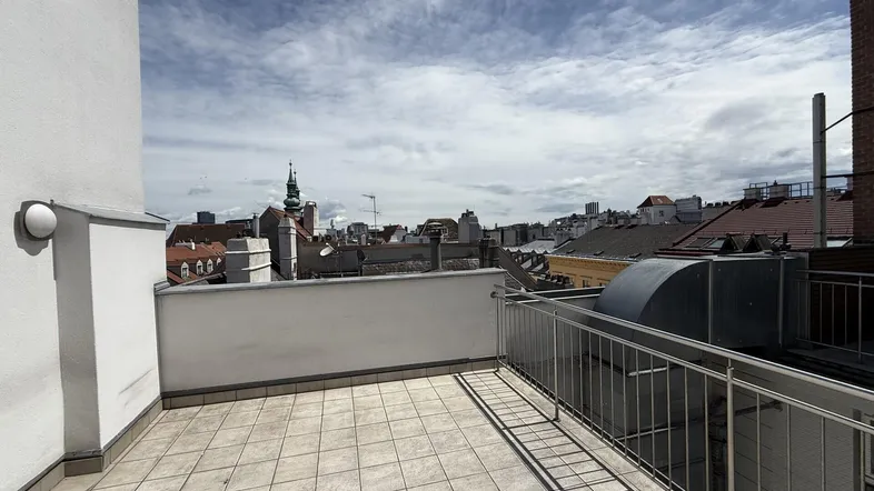 Geräumige Dachterrasse mit Fliesenboden und Metallgeländer bietet einen weiten Blick über die Stadt.