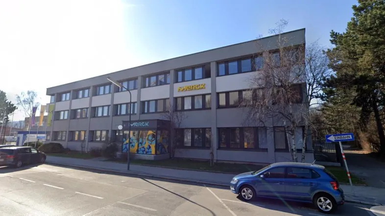 Gebäudeansicht eines modernen Bürokomplexes mit Parkplätzen und umliegender Vegetation unter blauem Himmel.