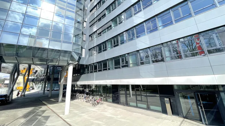 Moderne Bürogebäude-Fassade mit Glas- und Metallverkleidung, Fahrradständern und Eingangsbereich unter blauem Himmel.