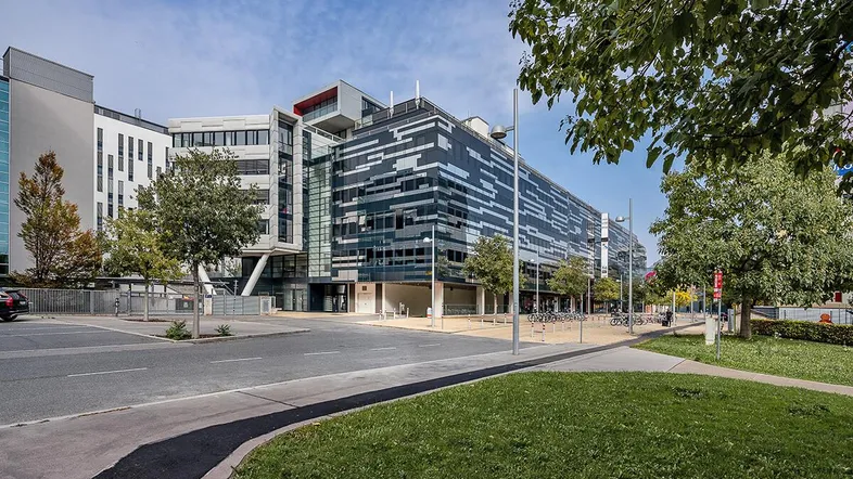 Modernes Bürogebäude mit auffälliger Fassadengestaltung, umgeben von Bäumen und einer Straße an einem sonnigen Tag.