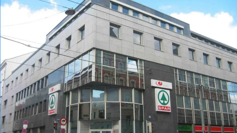 Modernes Geschäftsgebäude mit Glasfassade und Einzelhandelsflächen im Erdgeschoss an einer städtischen Straße.