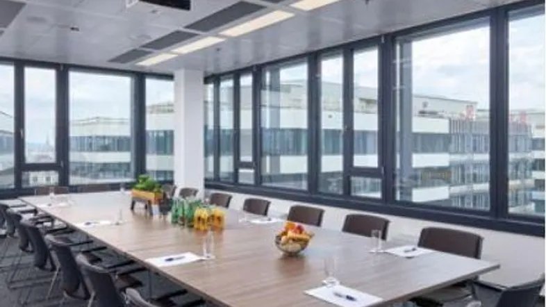 Geräumiger Konferenzraum mit großem Tisch, vielen Stühlen und weitreichendem Stadtblick durch die Fenster.