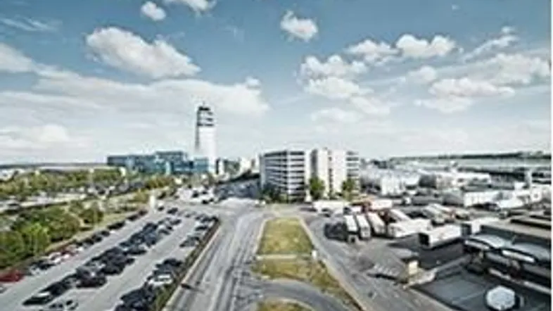 Luftaufnahme eines Gewerbegebiets mit Bürogebäuden, großen Parkplätzen und Zufahrtsstraßen unter blauem Himmel.