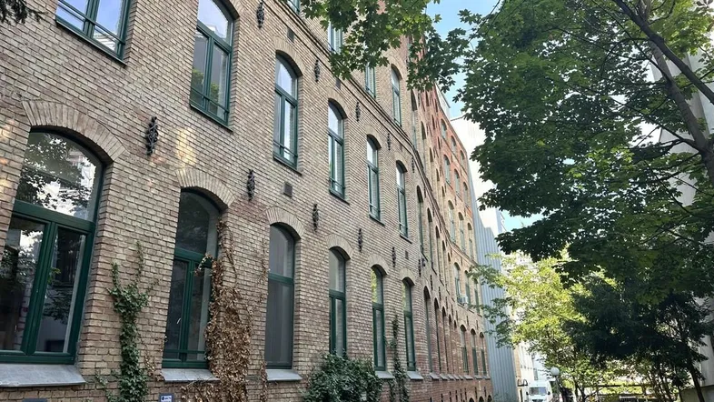 Historisches Backsteingebäude mit grünen Fensterrahmen und Efeu an der Fassade, umgeben von Bäumen.