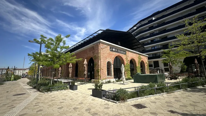 Historisches Backsteingebäude mit modernen Anbauten und einer sonnigen Außenterrasse unter blauem Himmel.