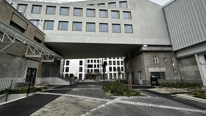 Moderne Gebäudefassade mit einem Durchgang und mehreren Etagen, umgeben von einer gepflasterten Zufahrt.
