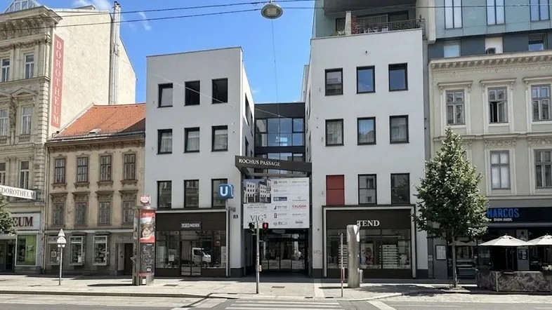 Moderne Geschäftsfassade mit großen Fenstern und einer Passage in einer städtischen Umgebung.