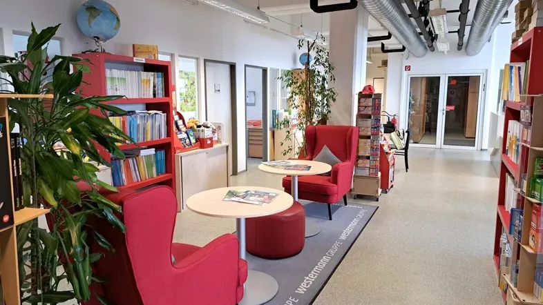Gemütlicher Loungebereich mit roten Sesseln, Bücherregalen und Pflanzen in einem modernen Bürogebäude.