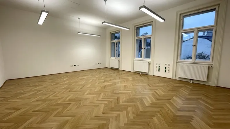 Geräumiger, leerer Büroraum mit Fischgrätparkett und großen Fenstern, ideal für verschiedene Nutzungen.