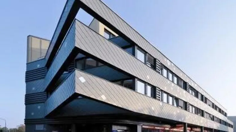 Modernes Gebäude mit markanter, abgewinkelter Fassade und großen Fenstern, unter klarem Himmel.