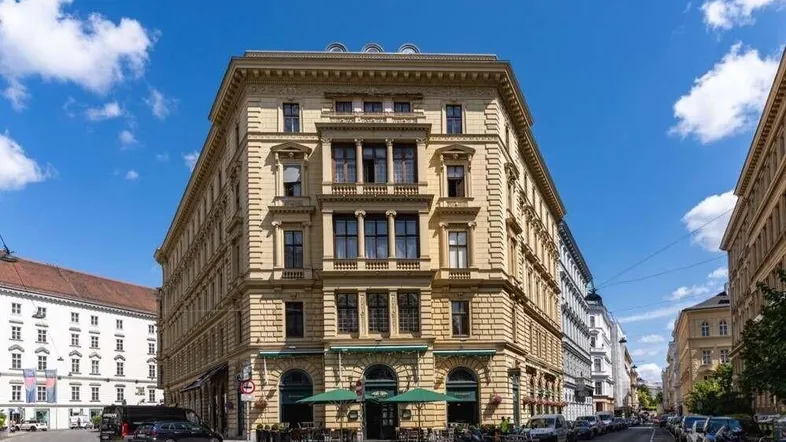 Historisches Gebäude an einer Straßenecke mit klassischer Architektur und Außengastronomie unter blauem Himmel.