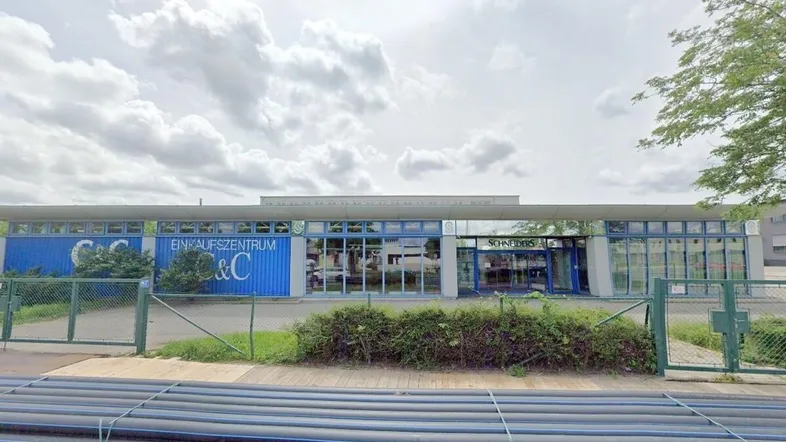 Außenansicht eines modernen Einkaufszentrums mit großer Glasfassade unter bewölktem Himmel.