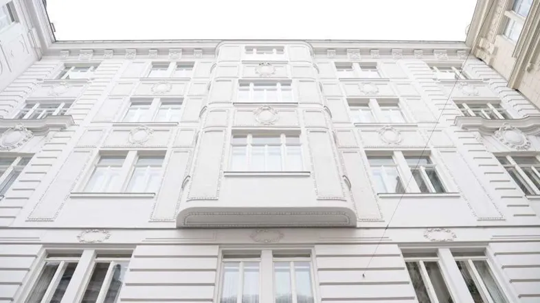 Eindrucksvolle weiße Fassade eines Altbaus mit vielen Fenstern und dekorativen Elementen.