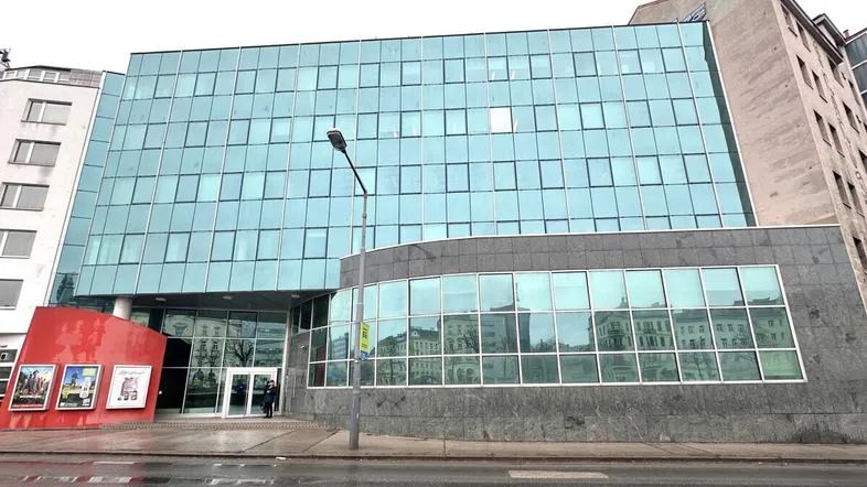 Modernes Bürogebäude mit großer Glasfassade und grauen Steinelementen an einem bewölkten Tag.