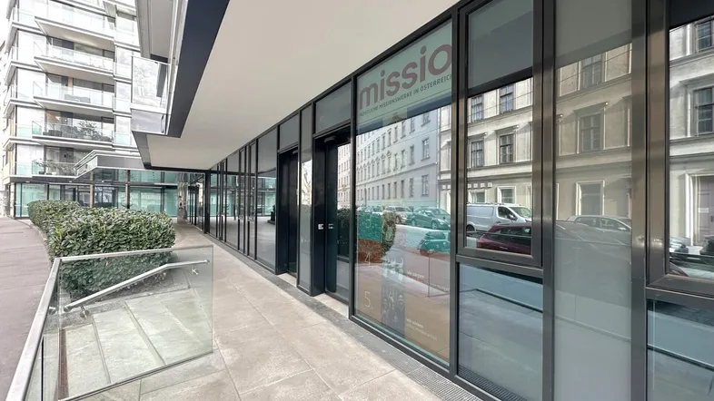 Moderne Geschäftsfassade mit großen Glasfenstern und einem gepflegten Eingangsbereich in urbaner Umgebung.