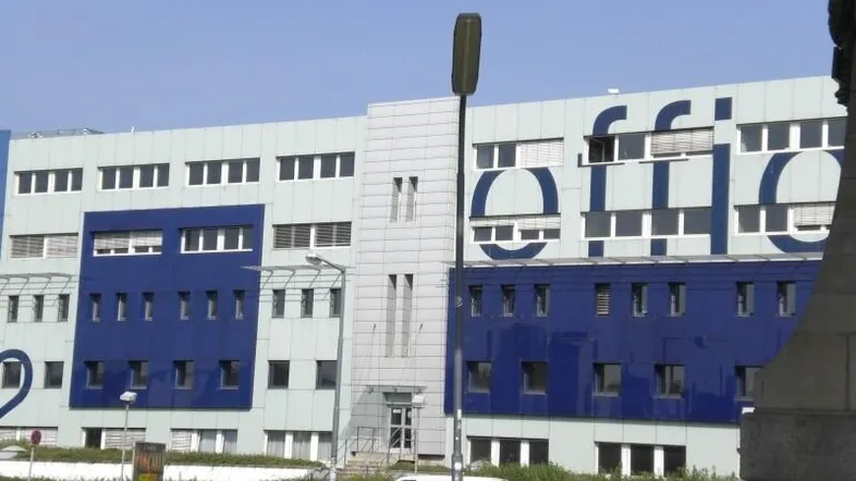 Moderne Bürogebäude-Fassade mit blauen und hellgrauen Paneelen und zahlreichen Fenstern.