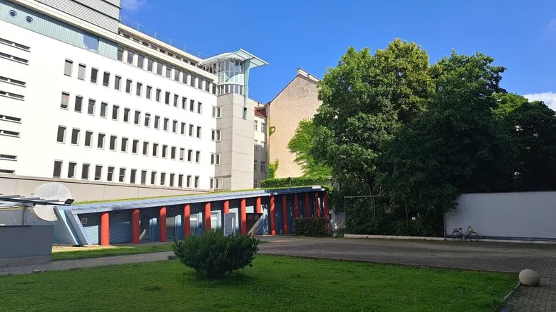 Außenansicht eines modernen Gebäudes mit Grünfläche, Bäumen und einem blauen Himmel an einem sonnigen Tag.