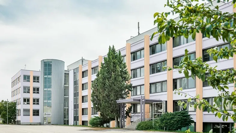 Modernes Bürogebäude mit Glasfassade und gepflegter Außenanlage unter bewölktem Himmel.