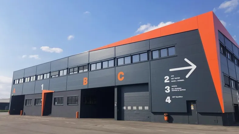 Modernes Logistikgebäude mit dunkelgrauer Fassade und orangefarbenen Akzenten unter blauem Himmel.