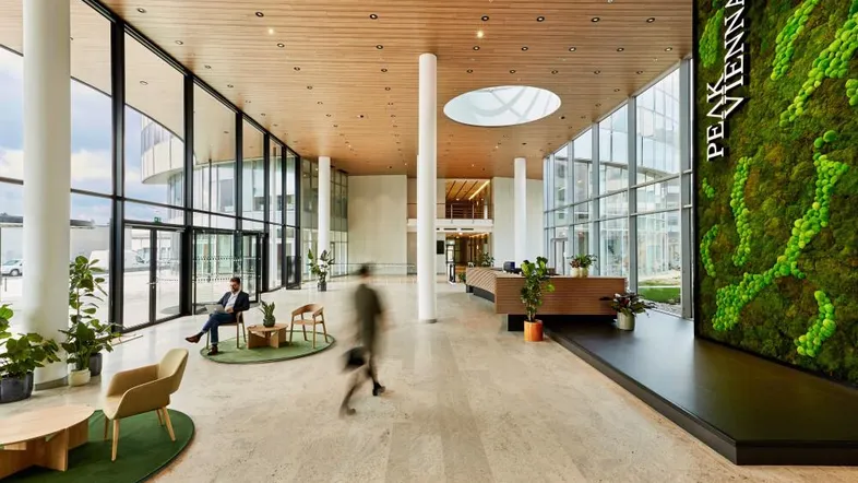Geräumige und moderne Lobby mit hohen Decken, großen Glasfronten und einer begrünten Wand.