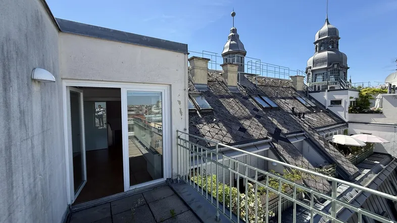 Geräumige Dachterrasse mit Blick auf die umliegenden Dächer und historische Türme unter blauem Himmel.