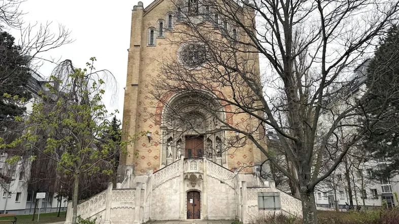 Historisches Kirchengebäude mit beeindruckender Fassade und Freitreppe, umgeben von Bäumen und Grünflächen.
