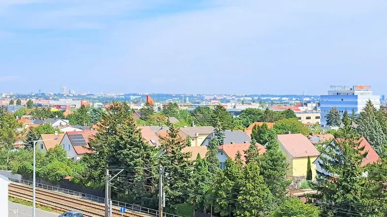 Weitblick über eine Wohnsiedlung mit vielen Bäumen, Bahngleisen und einer Stadtkulisse am Horizont.