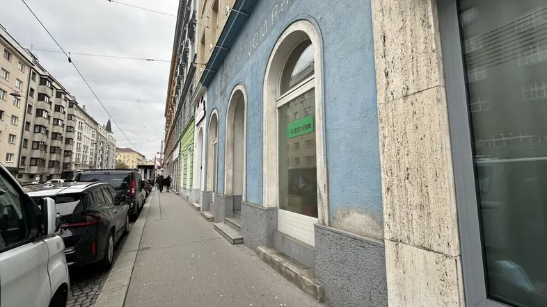 Blick auf die Fassade eines Gebäudes mit blauer Farbe und großen Bogenfenstern entlang einer belebten Straße.