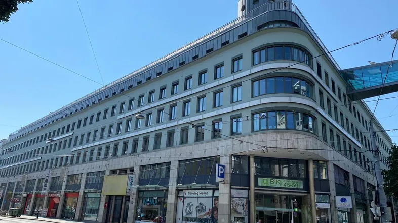 Modernes Geschäftsgebäude mit mehreren Etagen, großen Fenstern und einer geschwungenen Fassade an einer belebten Straße.
