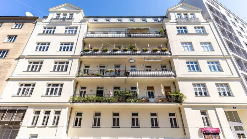 Klassisches Mehrfamilienhaus mit mehreren Balkonen und großen Fenstern in einer städtischen Umgebung.
