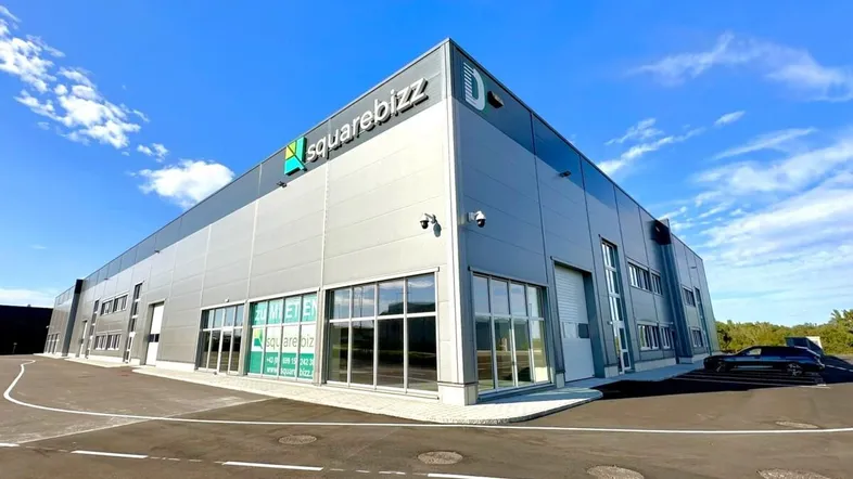 Modernes Gewerbegebäude mit großen Fenstern und Rolltoren unter blauem Himmel.