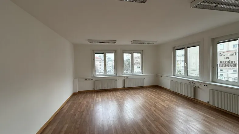 Geräumiger, leerer Raum mit Laminatboden und mehreren Fenstern, ideal als Bürofläche.