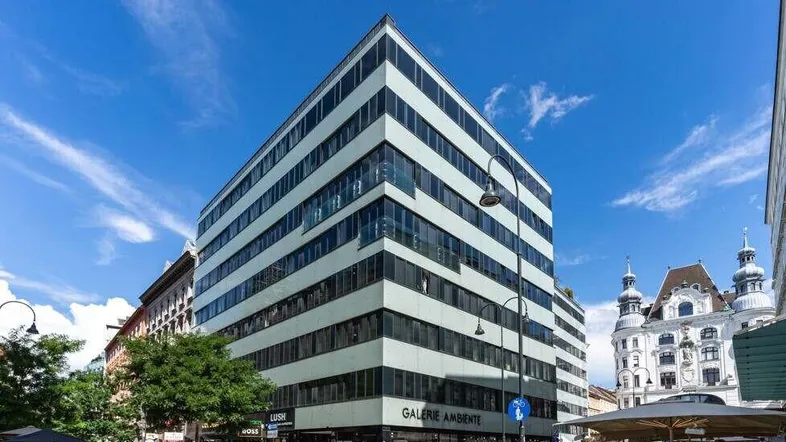 Modernes Bürogebäude mit Glasfassade und Geschäften im Erdgeschoss unter blauem Himmel.