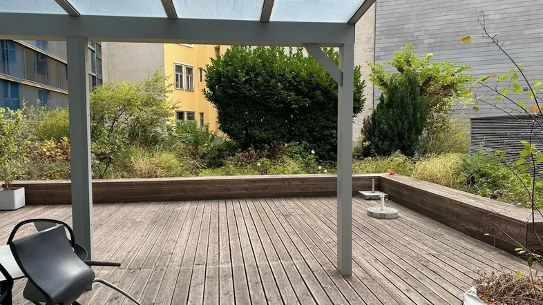 Geräumige Holzterrasse mit Glasüberdachung und Blick auf begrünte Innenhofbepflanzung.