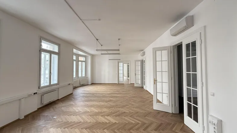 Geräumiges Büro mit Fischgrätparkett, hohen Decken und vielen Fenstern für natürliches Licht und Stadtblick.