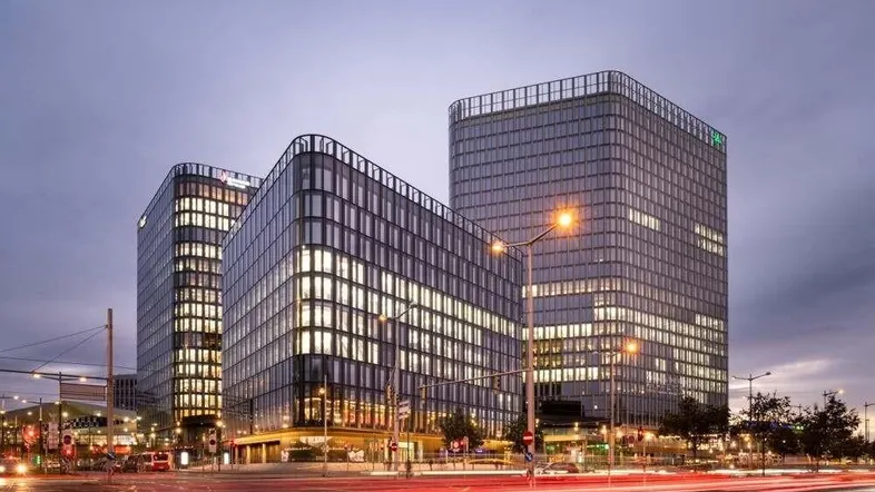 Moderne Bürogebäude mit Glasfassaden in der Dämmerung, umgeben von Stadtlichtern und Verkehr.