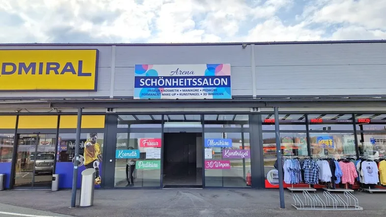 Vorderansicht eines Geschäftshauses mit großem "Schönheitssalon" Schild und weiteren Ladenfronten.