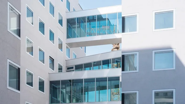 Moderne Gebäudefassade mit großen Fenstern und gläsernen Verbindungsbrücken zwischen den Gebäudeteilen.