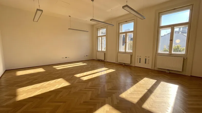 Heller Büroraum mit Fischgrätparkettboden, großen Fenstern und viel natürlichem Tageslicht, ideal für Arbeit.
