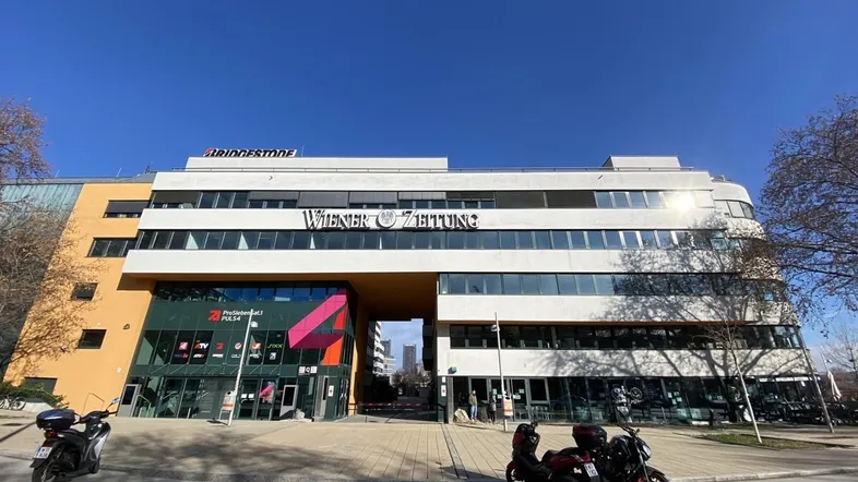 Moderne Bürogebäude-Fassade mit großen Fenstern und einem Durchgang, beleuchtet von der Sonne.