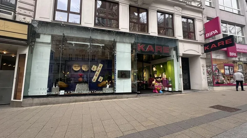 Fassade eines Geschäftsgebäudes mit großen Schaufenstern und darüberliegenden Wohnungen an einer belebten Straße.