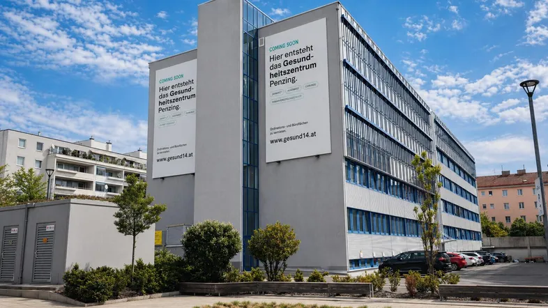 Seitenansicht eines modernen Gebäudes mit großen Werbebannern für ein entstehendes Gesundheitszentrum.