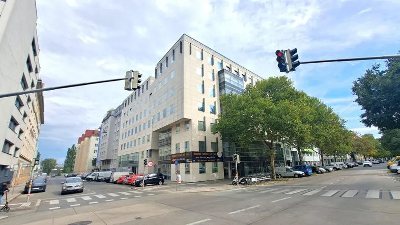 Modernes Bürogebäude an einer belebten Straßenkreuzung mit vielen Fenstern und geparkten Autos.